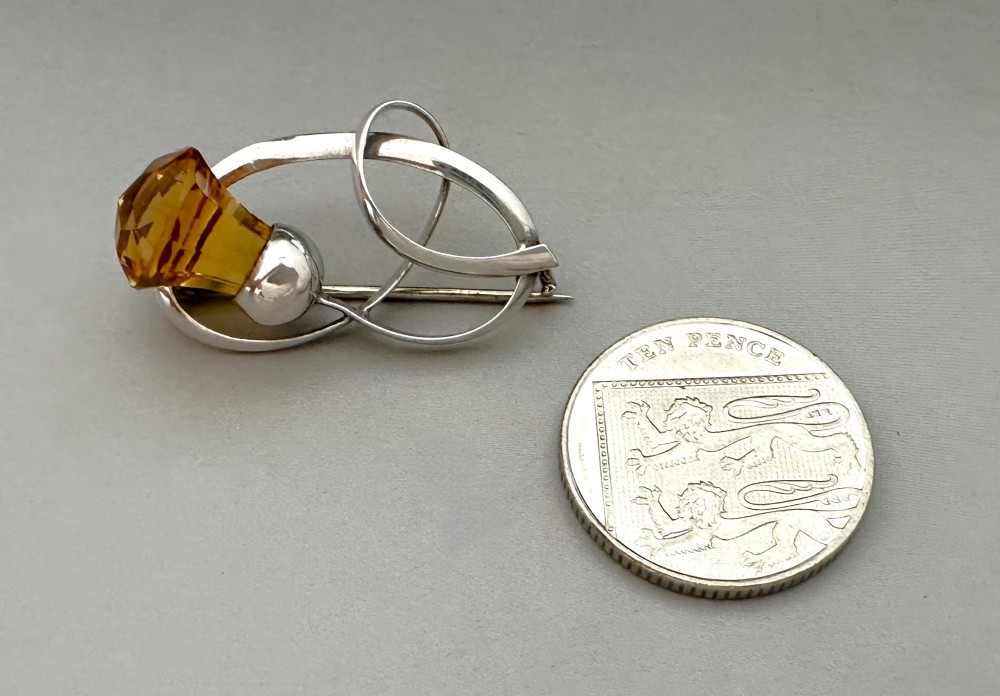 An Edwardian silver brooch designed in an openwork loop motif featuring a stylized Scottish thistle set with a faceted amber-coloured stone. View IV