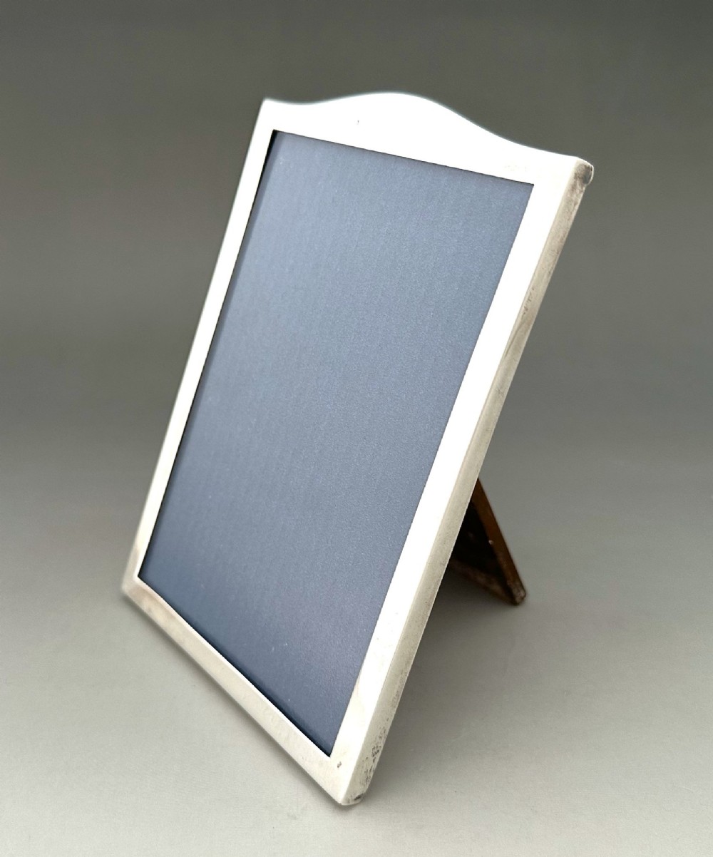 A rectangular sterling silver photo frame featuring a gently arched top edge, hallmark stamps along the side, and a dark blue insert. View II