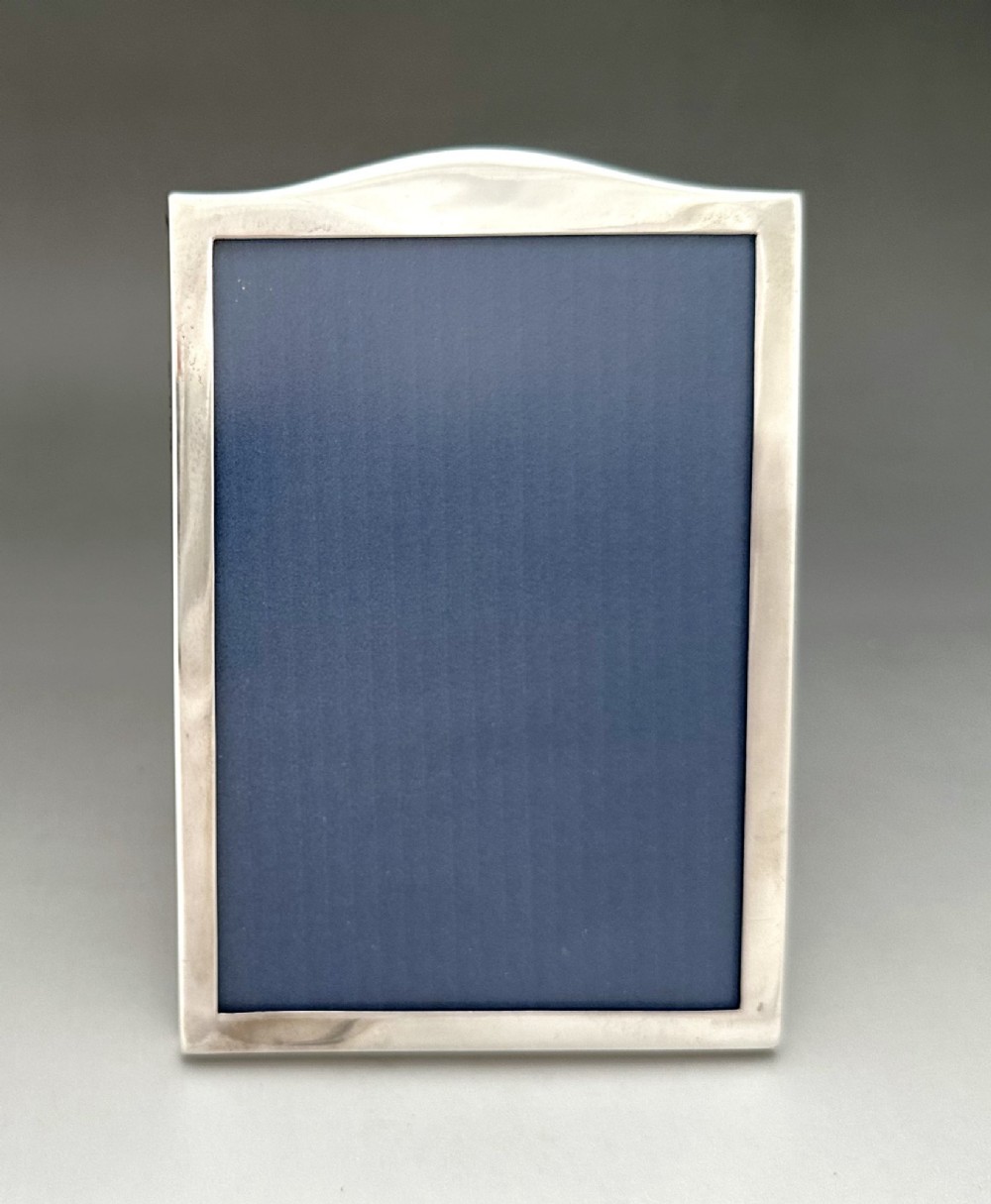 A rectangular sterling silver photo frame featuring a gently arched top edge, hallmark stamps along the side, and a dark blue insert. View V