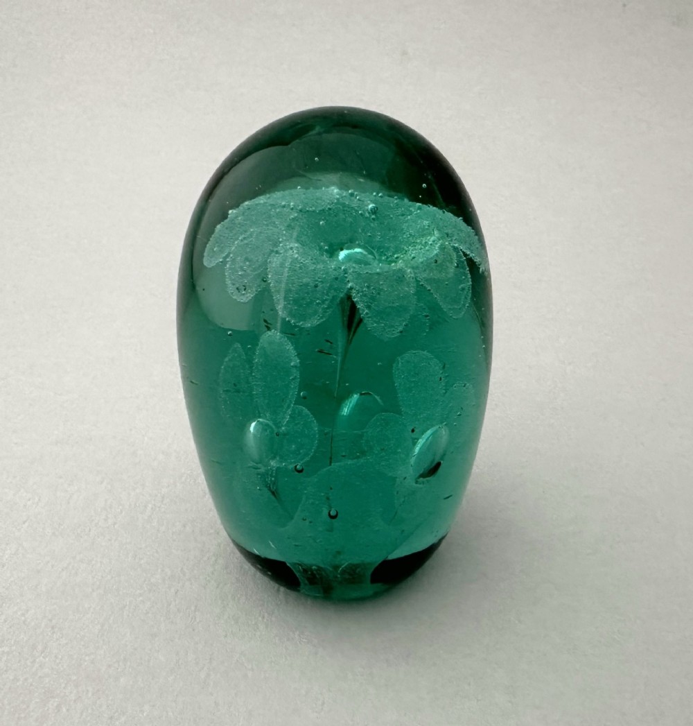 A heavy oval green glass paperweight displaying an internal controlled bubble floral motif.