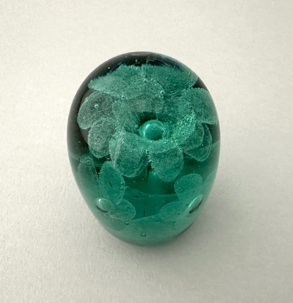 A heavy oval green glass paperweight displaying an internal controlled bubble floral motif. View II
