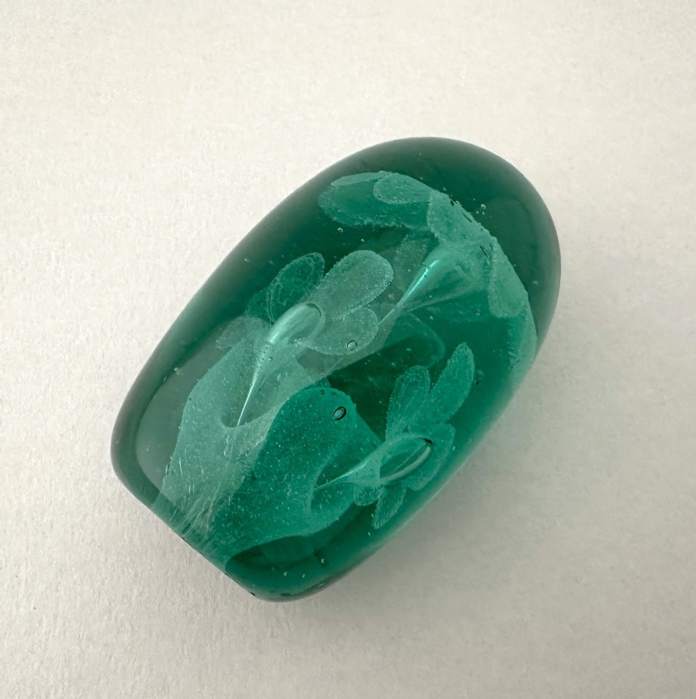 A heavy oval green glass paperweight displaying an internal controlled bubble floral motif. View IV