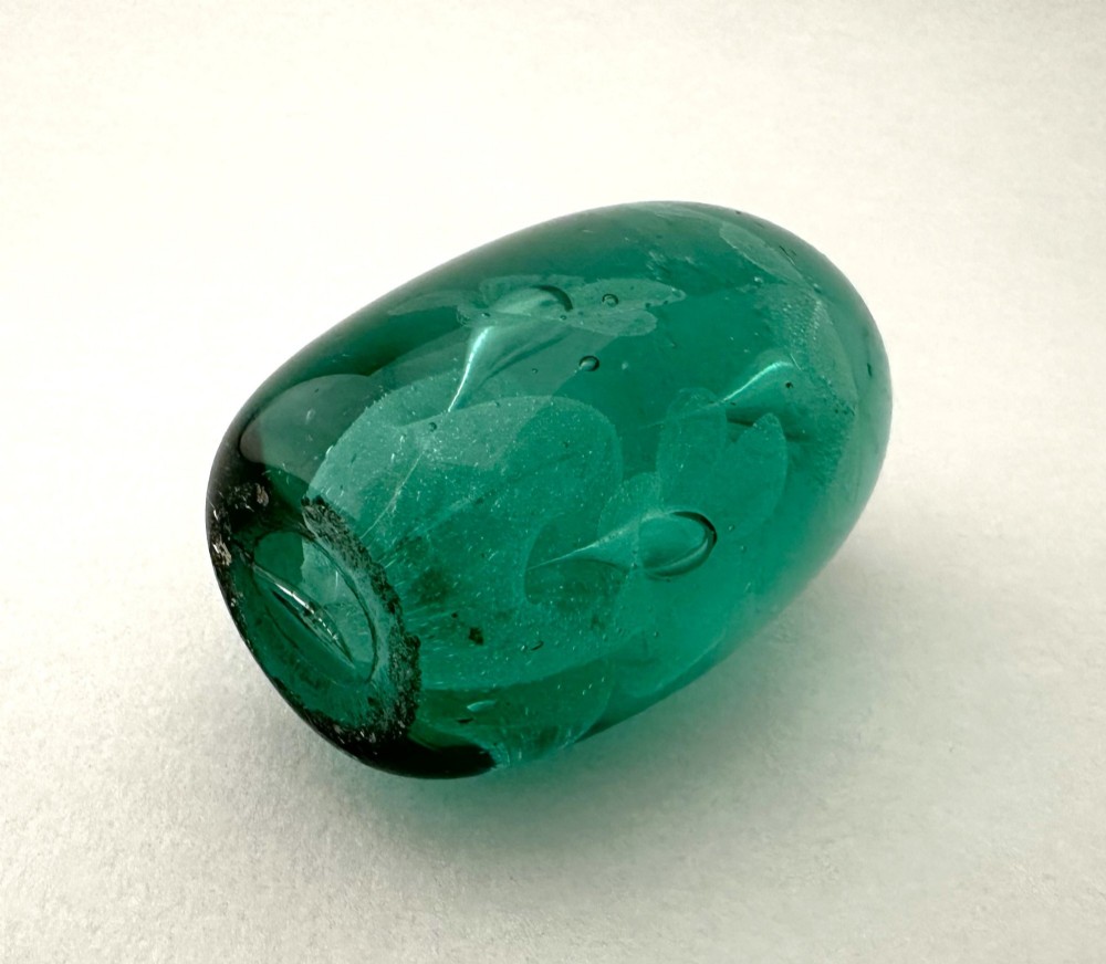 A heavy oval green glass paperweight displaying an internal controlled bubble floral motif. View V