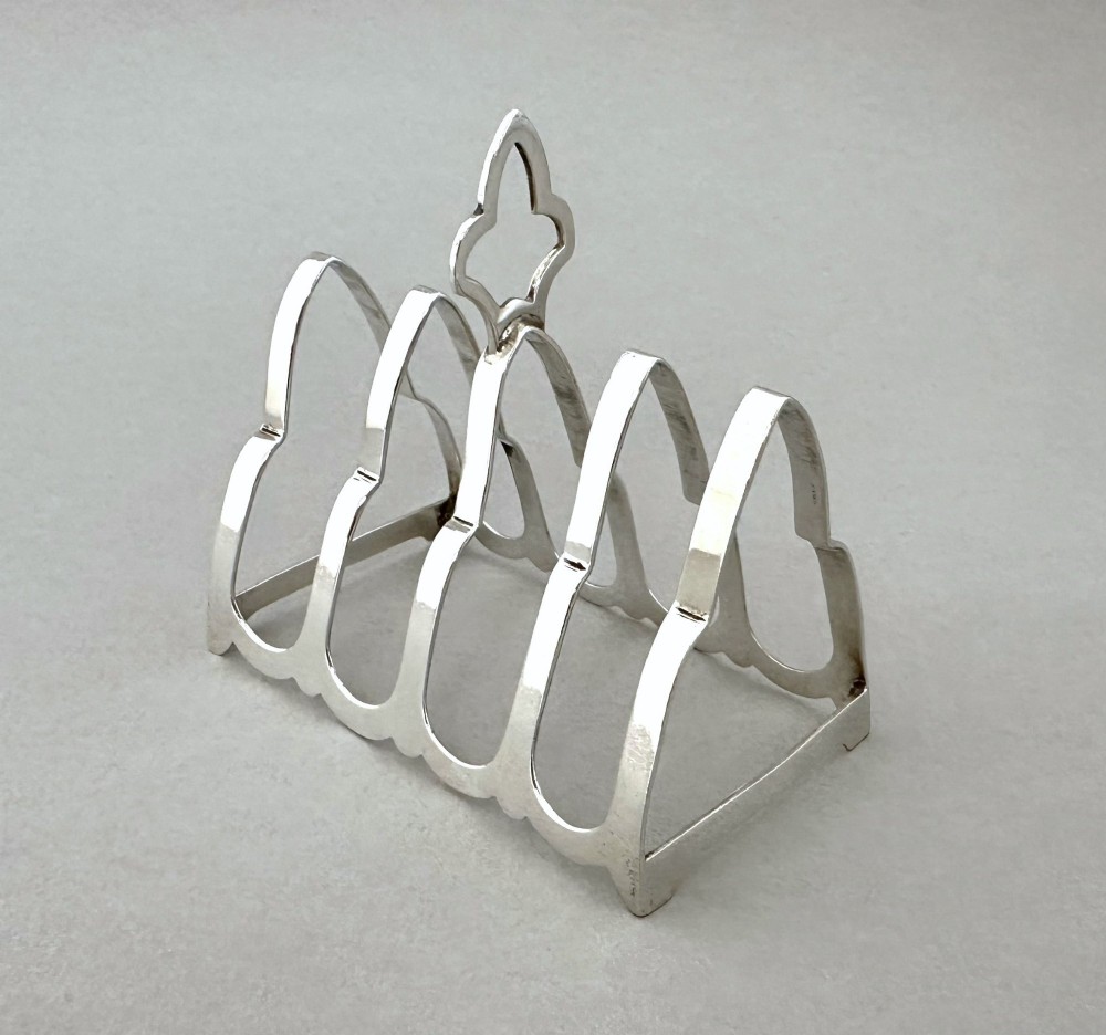 A hallmarked silver four-slice toast rack featuring shaped Gothic arch dividers and a central pierced top handle. View II