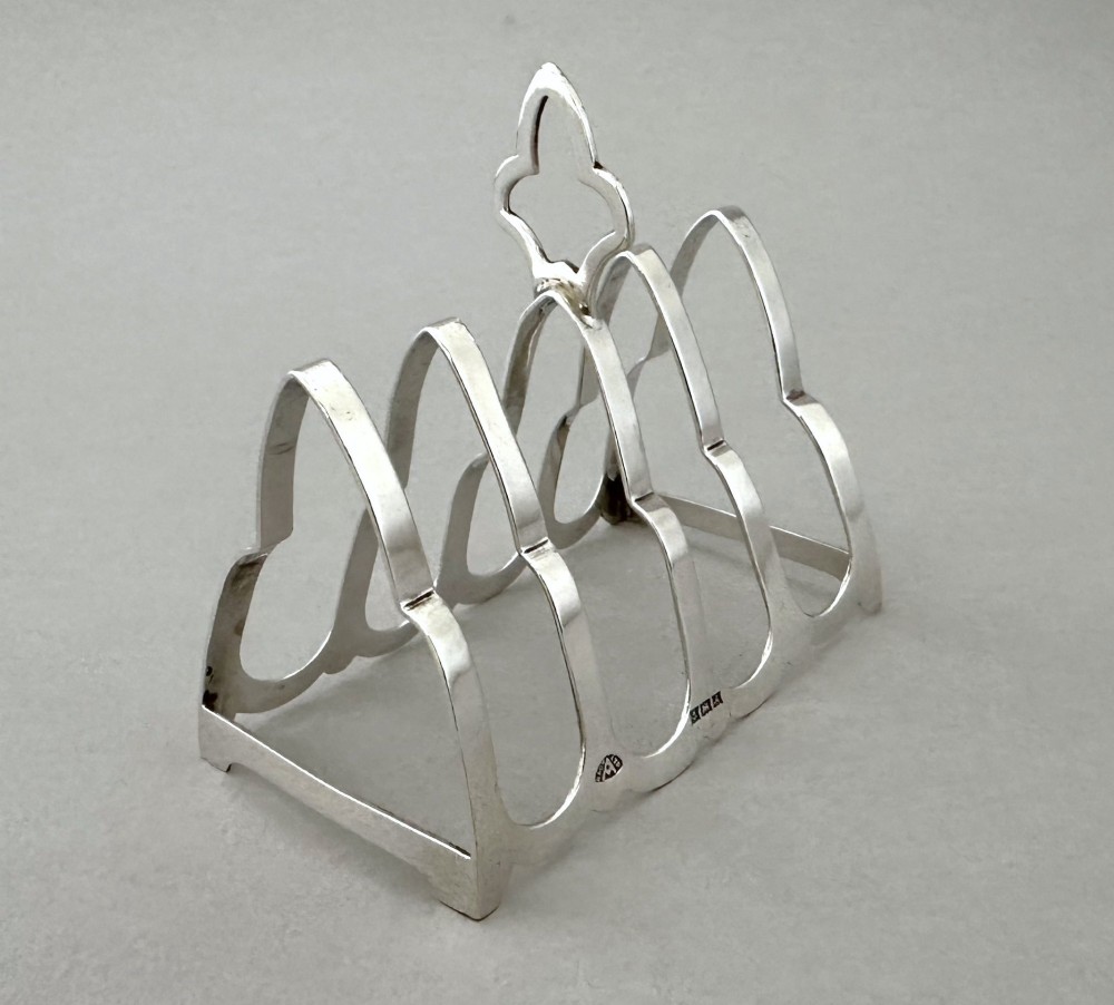A hallmarked silver four-slice toast rack featuring shaped Gothic arch dividers and a central pierced top handle.