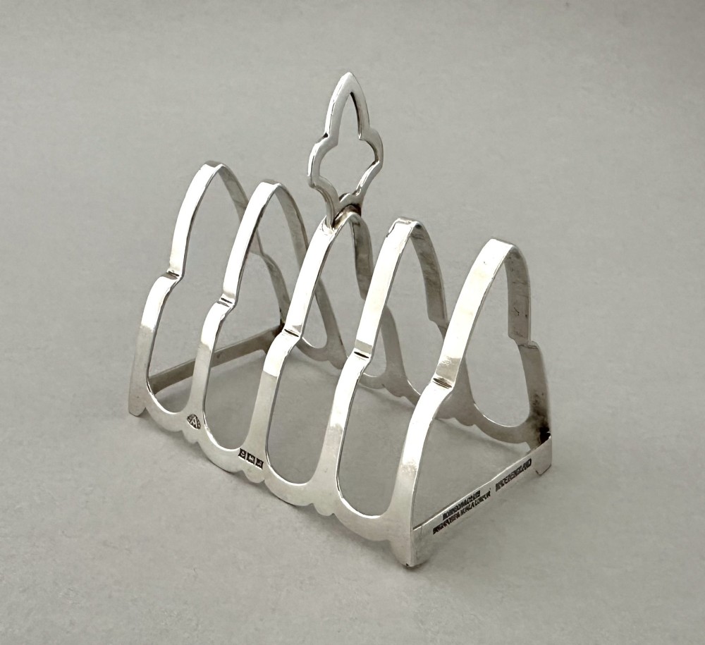 A hallmarked silver four-slice toast rack featuring shaped Gothic arch dividers and a central pierced top handle. View III