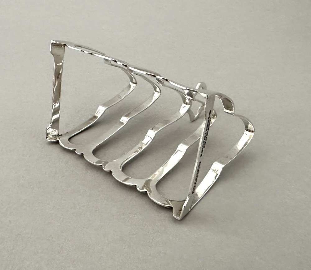 A hallmarked silver four-slice toast rack featuring shaped Gothic arch dividers and a central pierced top handle. View V