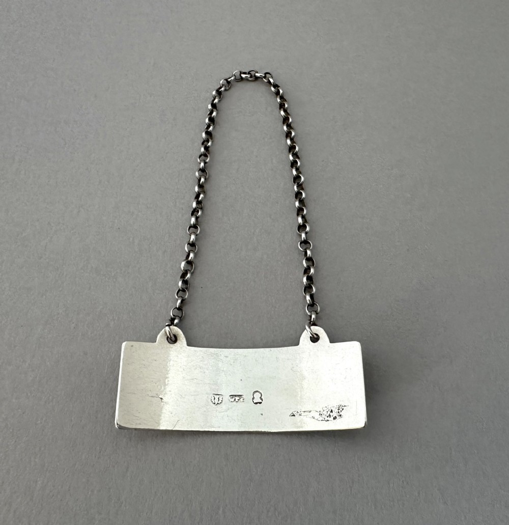 A rectangular silver decanter label engraved with the word PORT and suspended by a thin silver link chain. View II