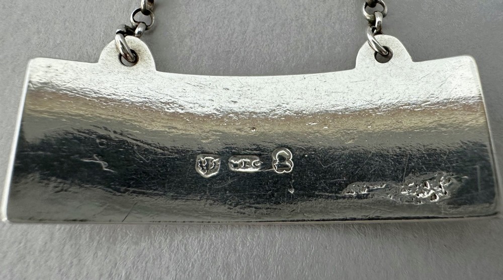 A rectangular silver decanter label engraved with the word PORT and suspended by a thin silver link chain. View III