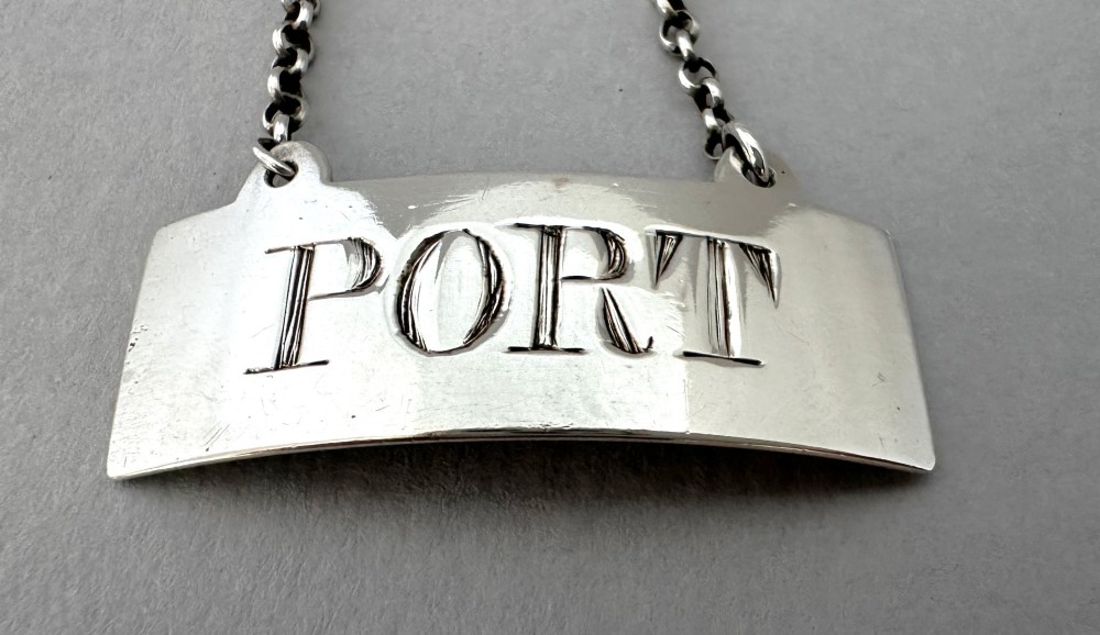 A rectangular silver decanter label engraved with the word PORT and suspended by a thin silver link chain. View IV