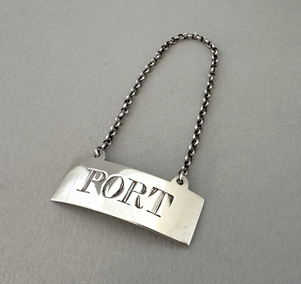 A rectangular silver decanter label engraved with the word PORT and suspended by a thin silver link chain. View V