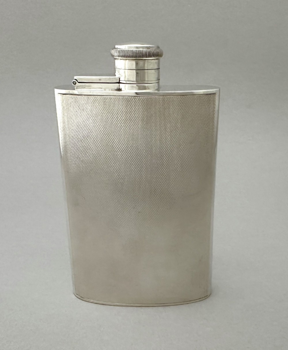 An Art Deco silver curved hip flask featuring fine engine-turned geometric detailing and a hinged cap.