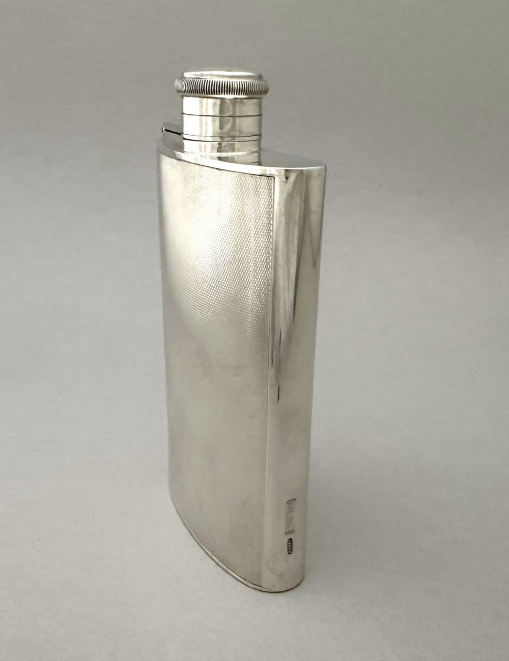 An Art Deco silver curved hip flask featuring fine engine-turned geometric detailing and a hinged cap. View III
