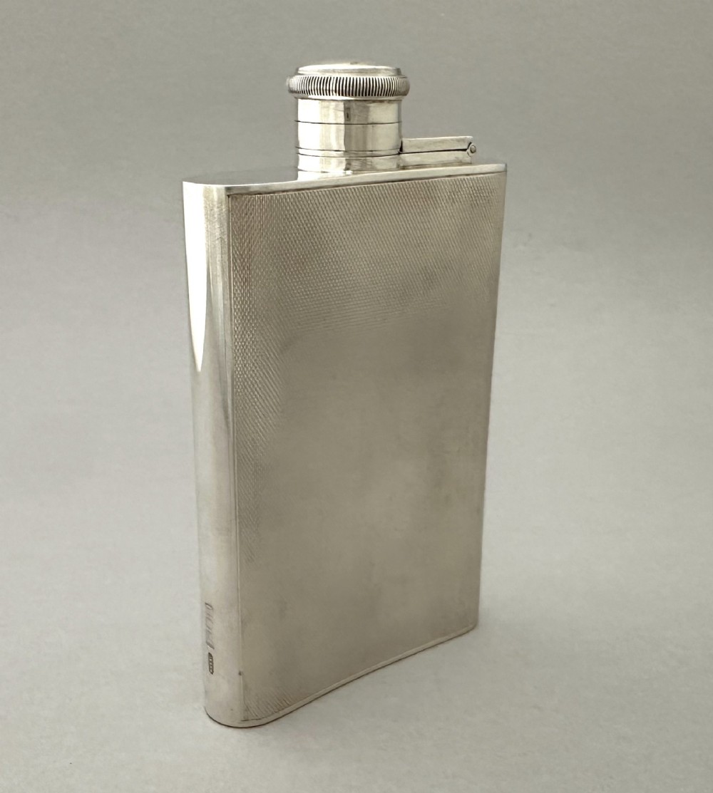 An Art Deco silver curved hip flask featuring fine engine-turned geometric detailing and a hinged cap. View IV