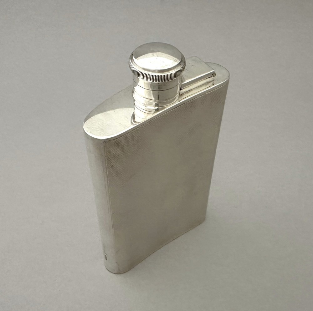 An Art Deco silver curved hip flask featuring fine engine-turned geometric detailing and a hinged cap. View V