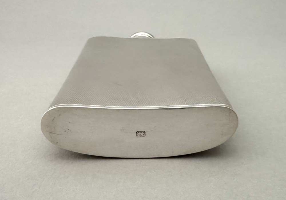 An Art Deco silver curved hip flask featuring fine engine-turned geometric detailing and a hinged cap. View VII