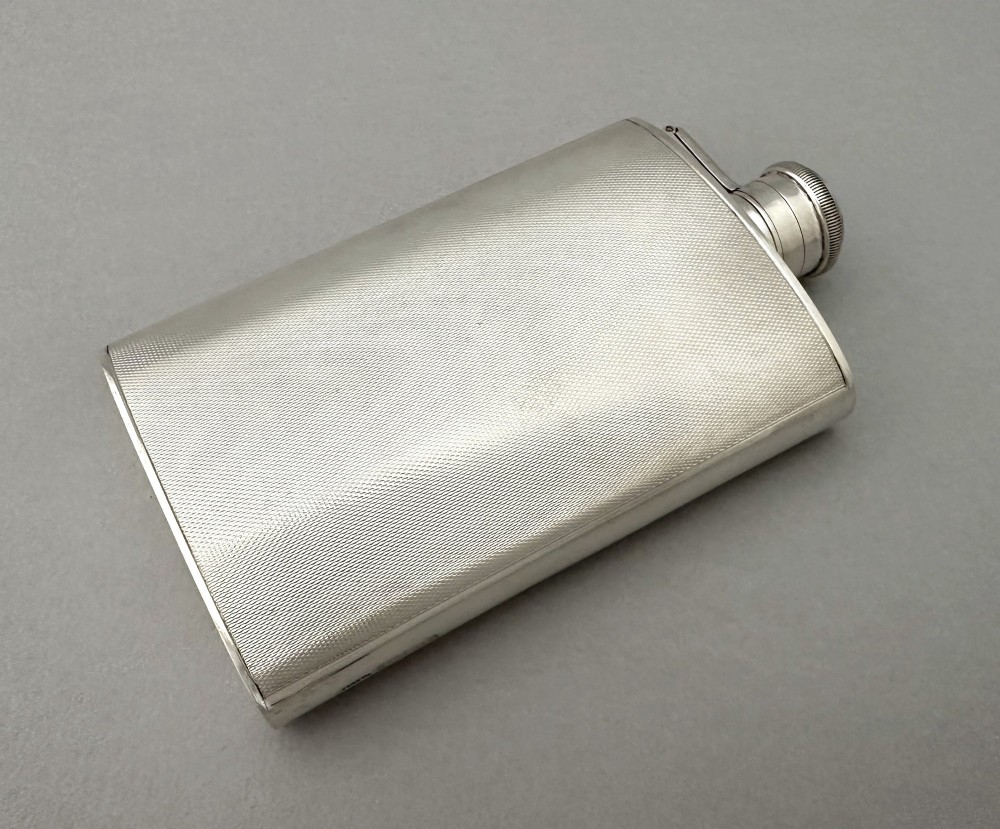 An Art Deco silver curved hip flask featuring fine engine-turned geometric detailing and a hinged cap. View VIII