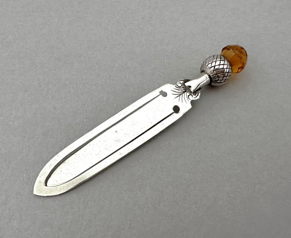 A silver bookmark clip with engraved leaf detailing, topped with an amber gemstone thistle terminal.