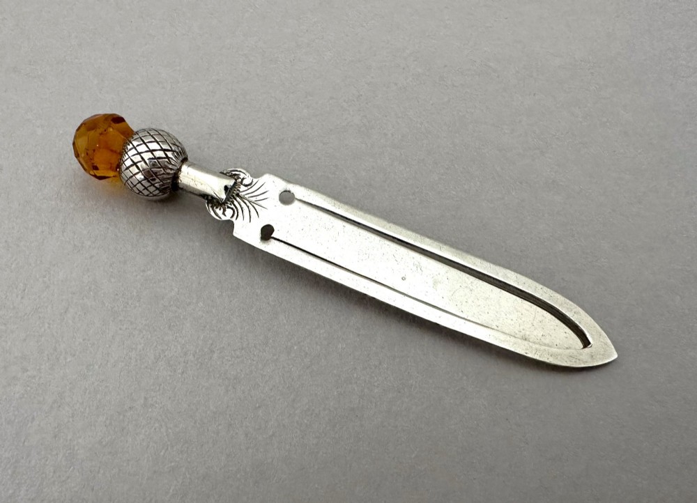 A silver bookmark clip with engraved leaf detailing, topped with an amber gemstone thistle terminal. View II