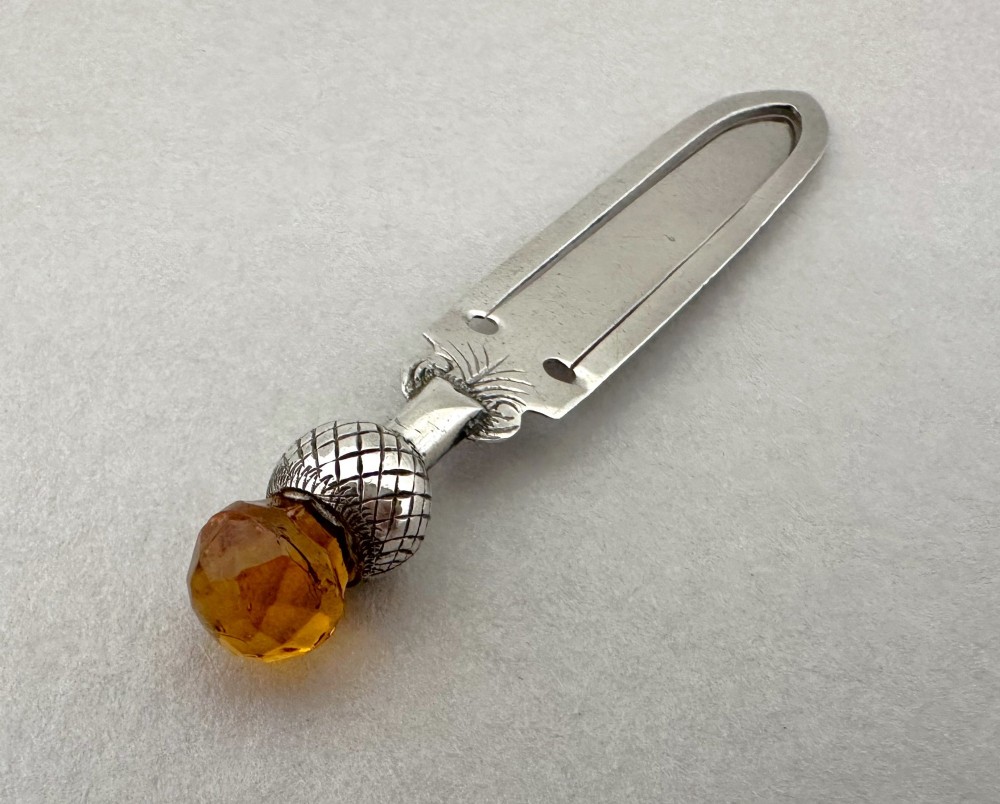 A silver bookmark clip with engraved leaf detailing, topped with an amber gemstone thistle terminal. View III