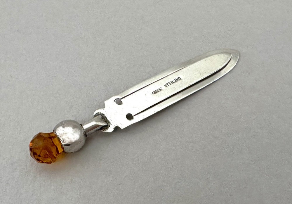 A silver bookmark clip with engraved leaf detailing, topped with an amber gemstone thistle terminal. View IV