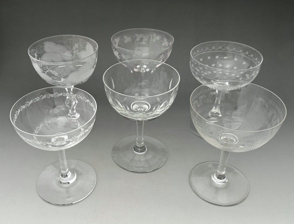 A harlequin set of six antique clear glass champagne coupes featuring various hand-etched geometric and floral patterns.