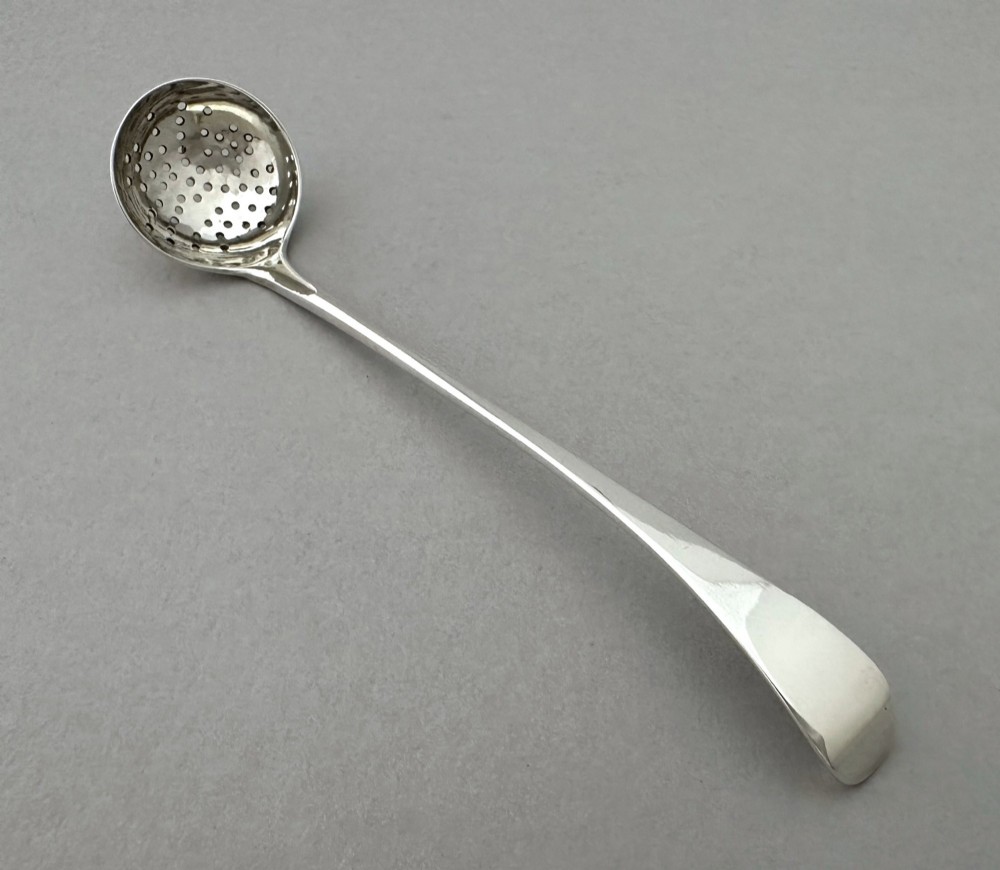 A Georgian sterling silver sifting ladle featuring a pierced round bowl and a smooth tapered handle.