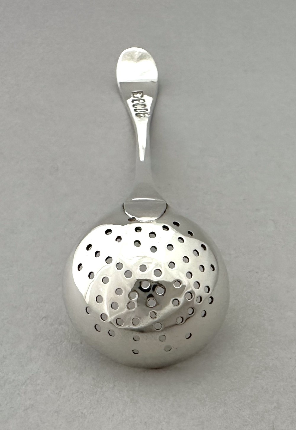 A Georgian sterling silver sifting ladle featuring a pierced round bowl and a smooth tapered handle. View V
