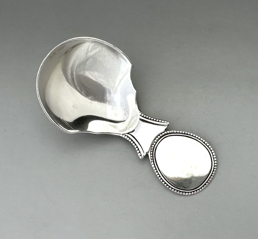A Regency sterling silver caddy spoon featuring a polished shovel bowl and an oval handle decorated with a beaded edge. View II