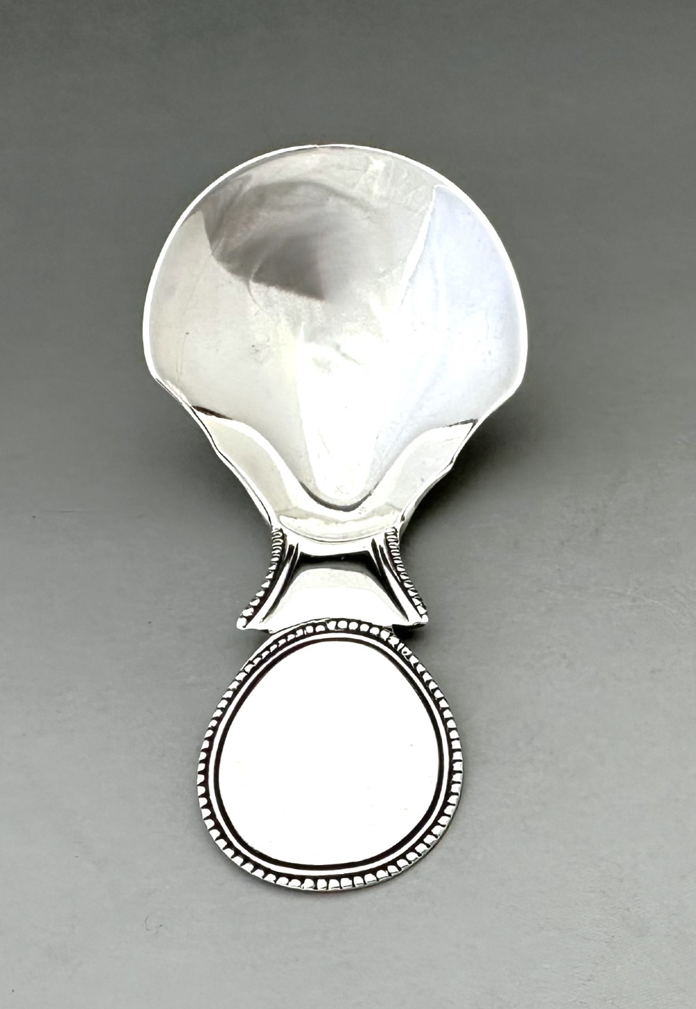 A Regency sterling silver caddy spoon featuring a polished shovel bowl and an oval handle decorated with a beaded edge. View V