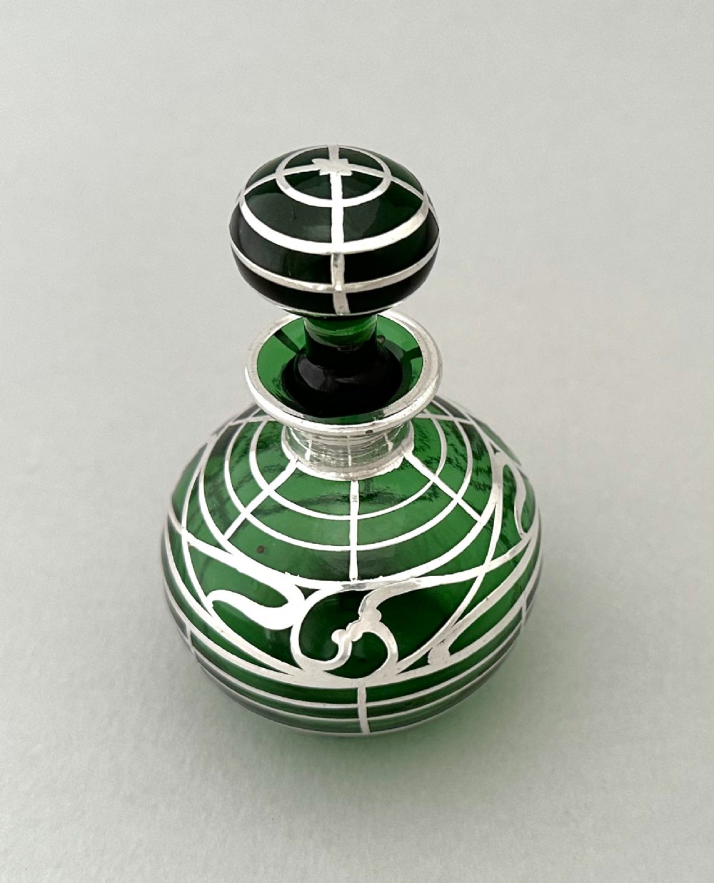 A globular green glass scent bottle featuring intricate silver overlay scrollwork and a matching fitted stopper. View II