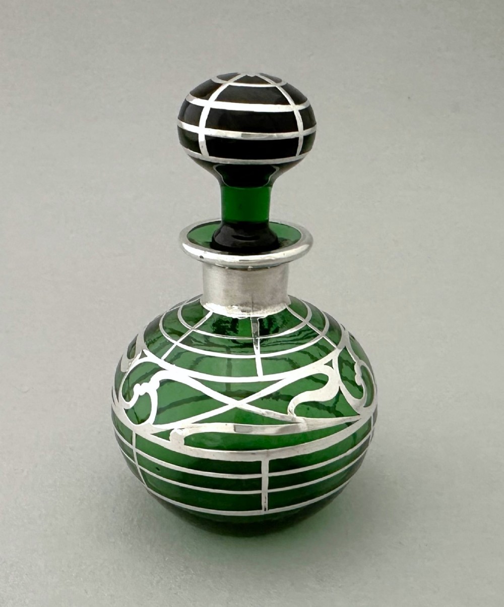 A globular green glass scent bottle featuring intricate silver overlay scrollwork and a matching fitted stopper. View III