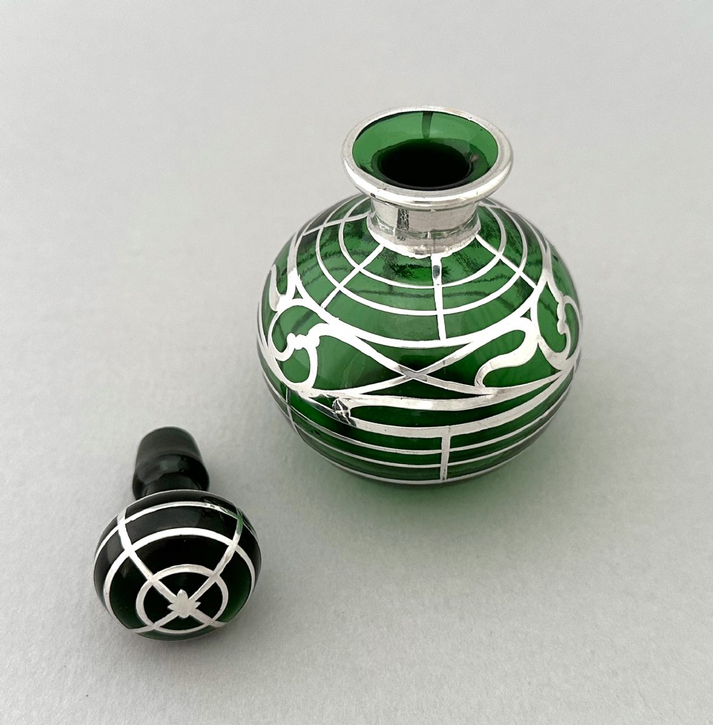 A globular green glass scent bottle featuring intricate silver overlay scrollwork and a matching fitted stopper. View IV