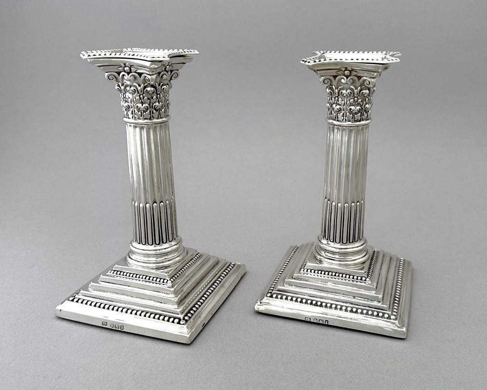 A pair of polished silver candlesticks crafted in the form of fluted Corinthian columns with acanthus capitals and stepped square bases. View II