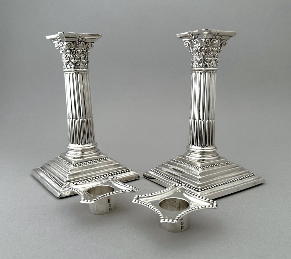 A pair of polished silver candlesticks crafted in the form of fluted Corinthian columns with acanthus capitals and stepped square bases. View V