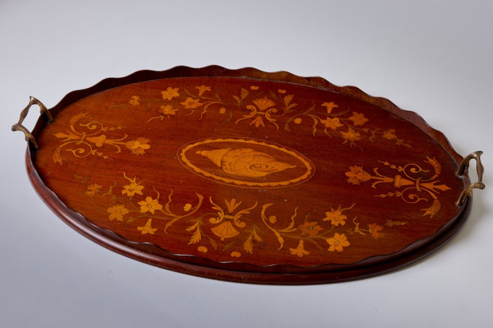 An oval mahogany serving tray featuring a scalloped rim, twin brass handles, floral marquetry, and a central inlaid shell motif.