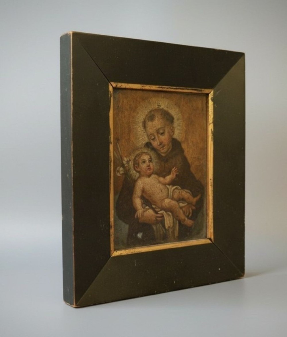 An antique Italian devotional icon depicting a saint holding the Christ Child set within a wide ebonised wooden frame with a gilded inner moulding. View II