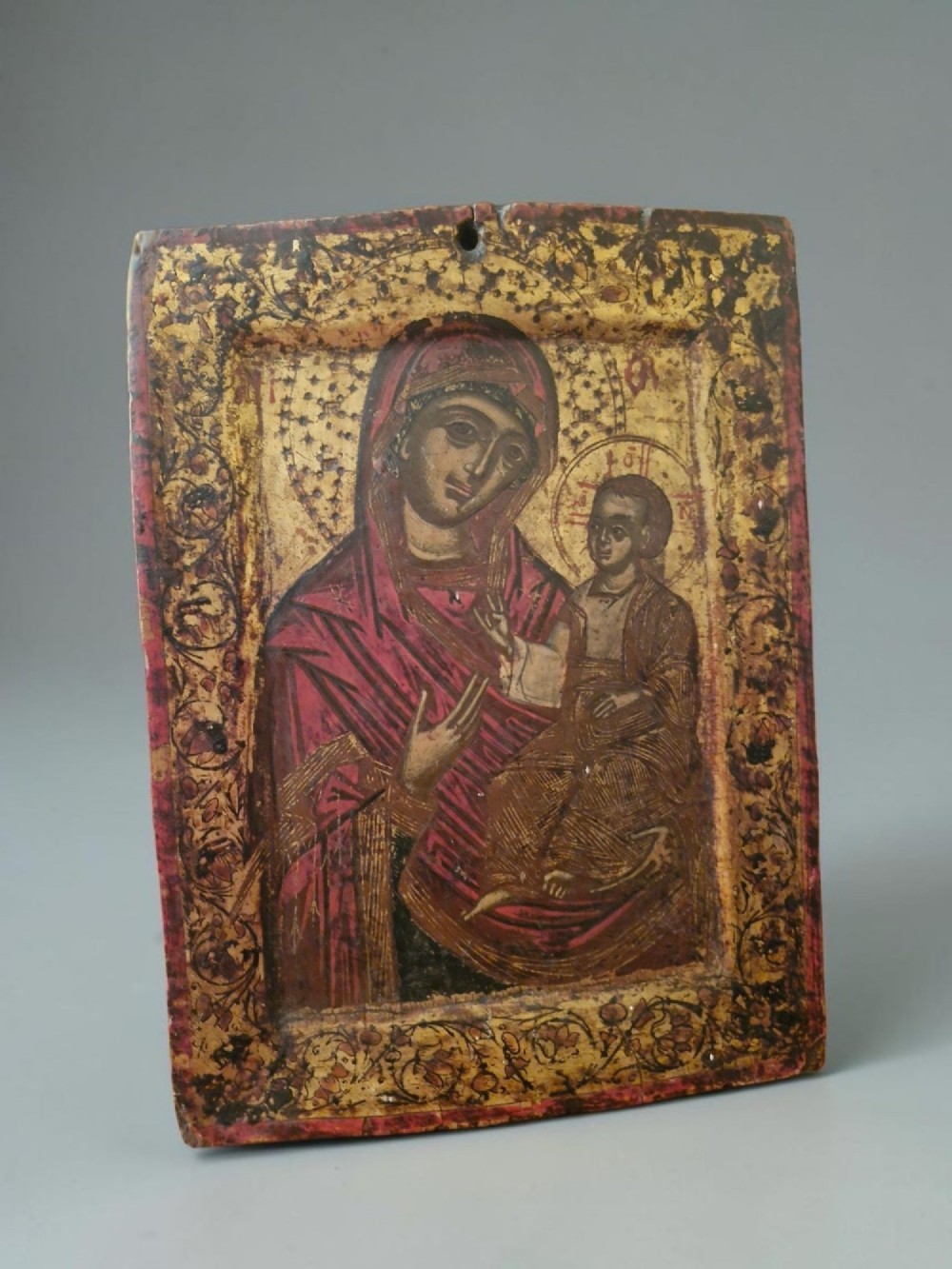 A rectangular wooden devotional icon panel featuring a gilded border and a painted depiction of the Virgin Mary holding the Christ Child.