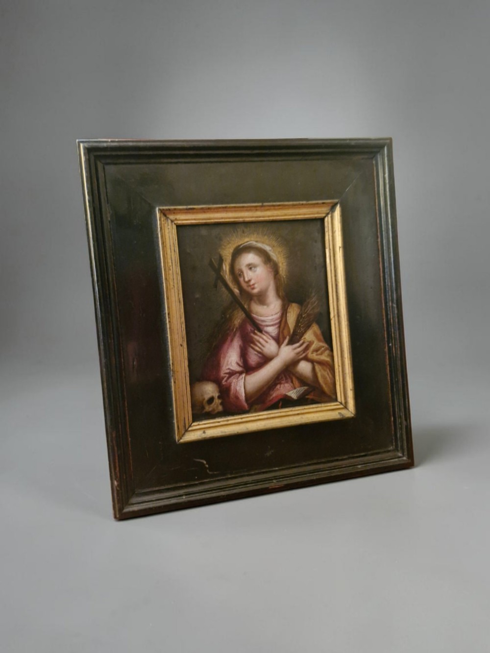 A small Flemish style religious oil painting depicting a female saint holding a cross and palm frond, housed in a thick ebonised wood frame with a gold sight edge. View II