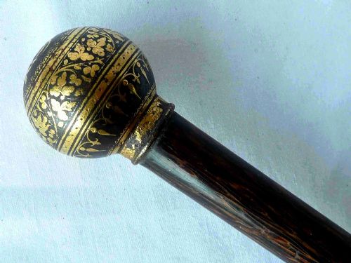 fig 1. An antique walking stick featuring a round steel ball handle with intricate gold damascene inlay mounted on a dark palm wood shaft.