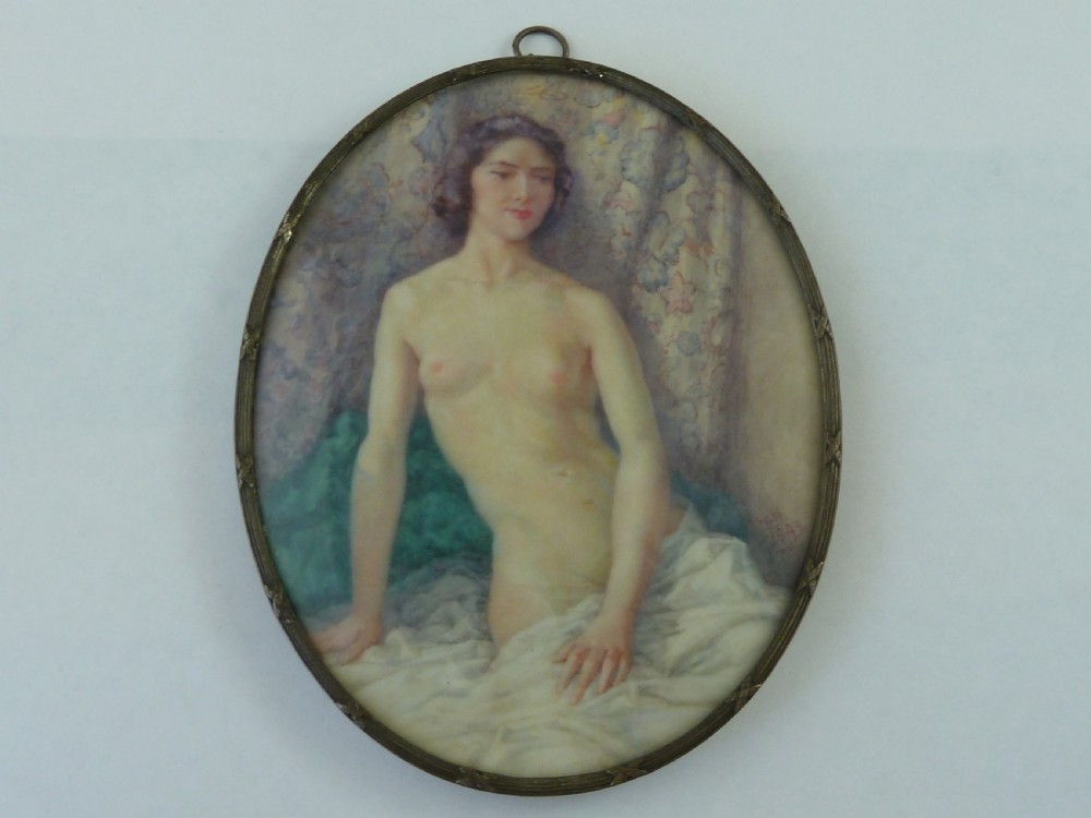 An oval hand-painted portrait miniature depicting a seated female nude resting on white drapery set in a thin metal frame.