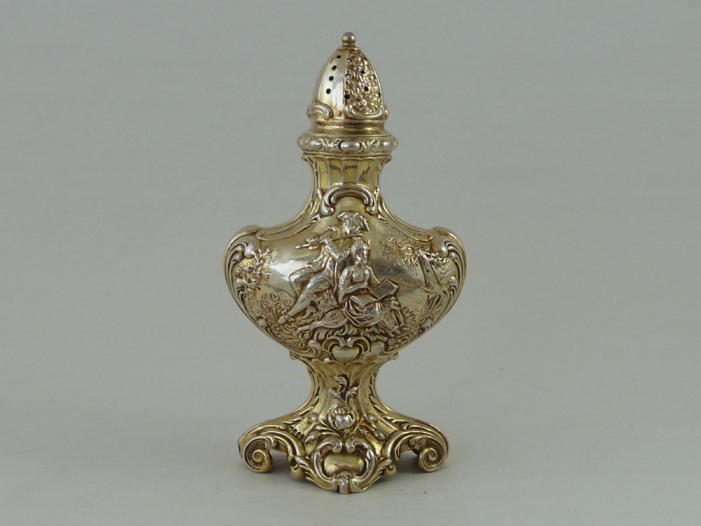 A Hanau silver gilt sugar caster featuring elaborate Rococo relief scenes of figures in a landscape and a pierced finial lid. View II