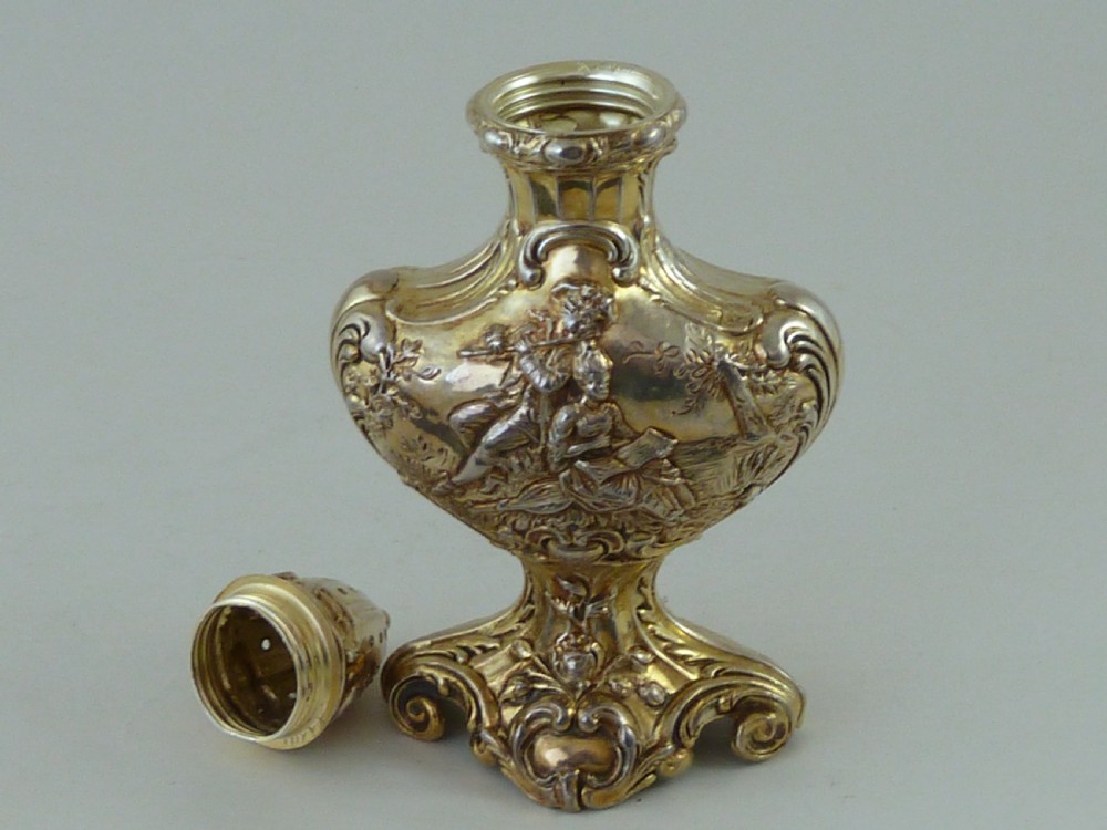 A Hanau silver gilt sugar caster featuring elaborate Rococo relief scenes of figures in a landscape and a pierced finial lid. View V