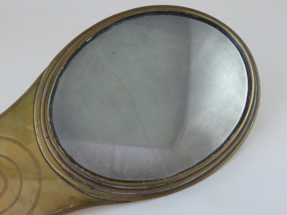 A paddle-shaped brass hand mirror displaying concentric engraved rings on its reverse casing. View VI