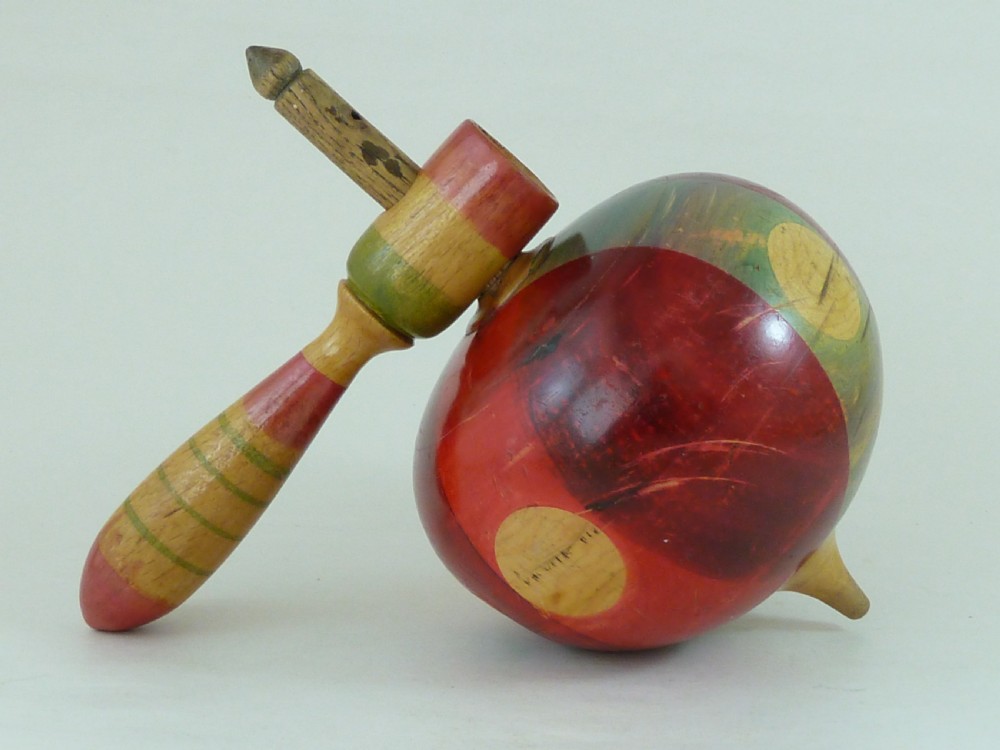 A turned wooden humming spinning top featuring polychrome painted bands in red, green, and yellow with an attached turned wooden handle.