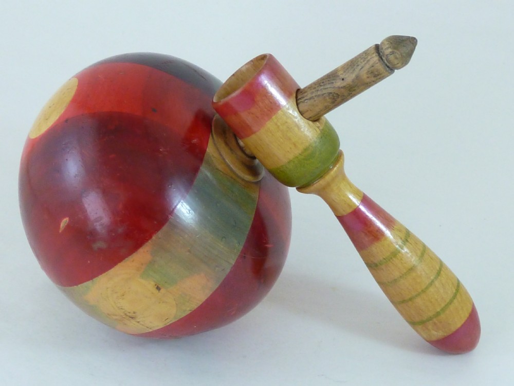 A turned wooden humming spinning top featuring polychrome painted bands in red, green, and yellow with an attached turned wooden handle. View II