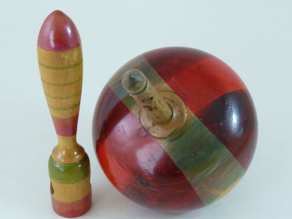 A turned wooden humming spinning top featuring polychrome painted bands in red, green, and yellow with an attached turned wooden handle. View VI