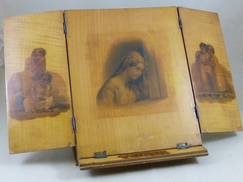 A Victorian Mauchline ware folding wooden reading stand in pale wood featuring black transfer prints of classical figures across three panels.