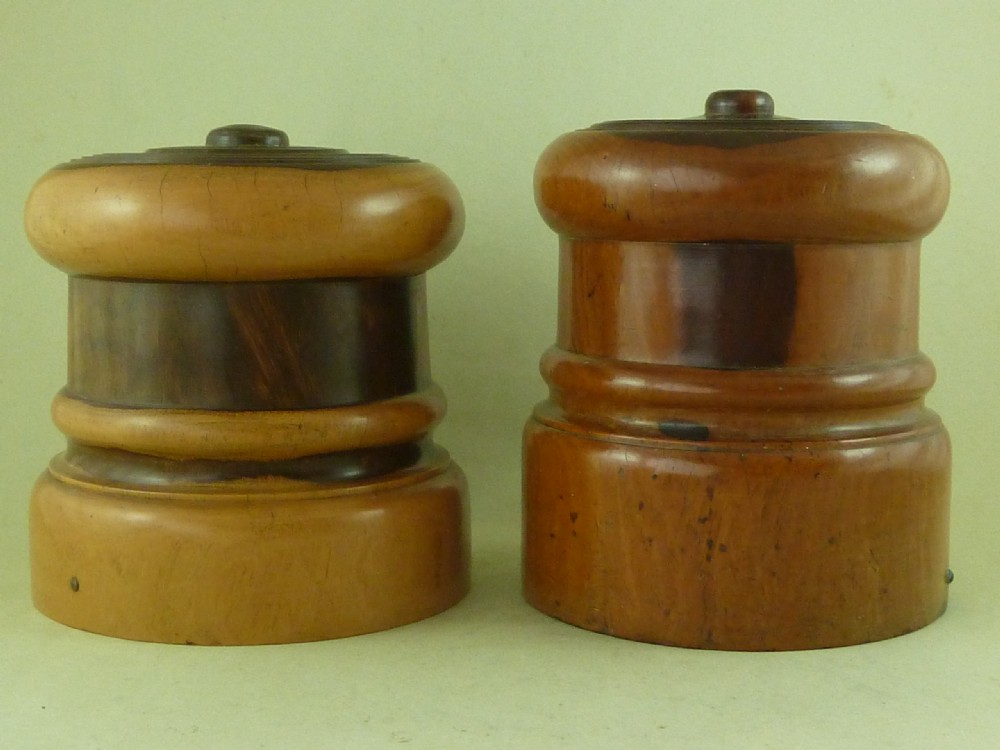 A near pair of turned lignum vitae wooden string holders with cylindrical barrels and rounded tops.