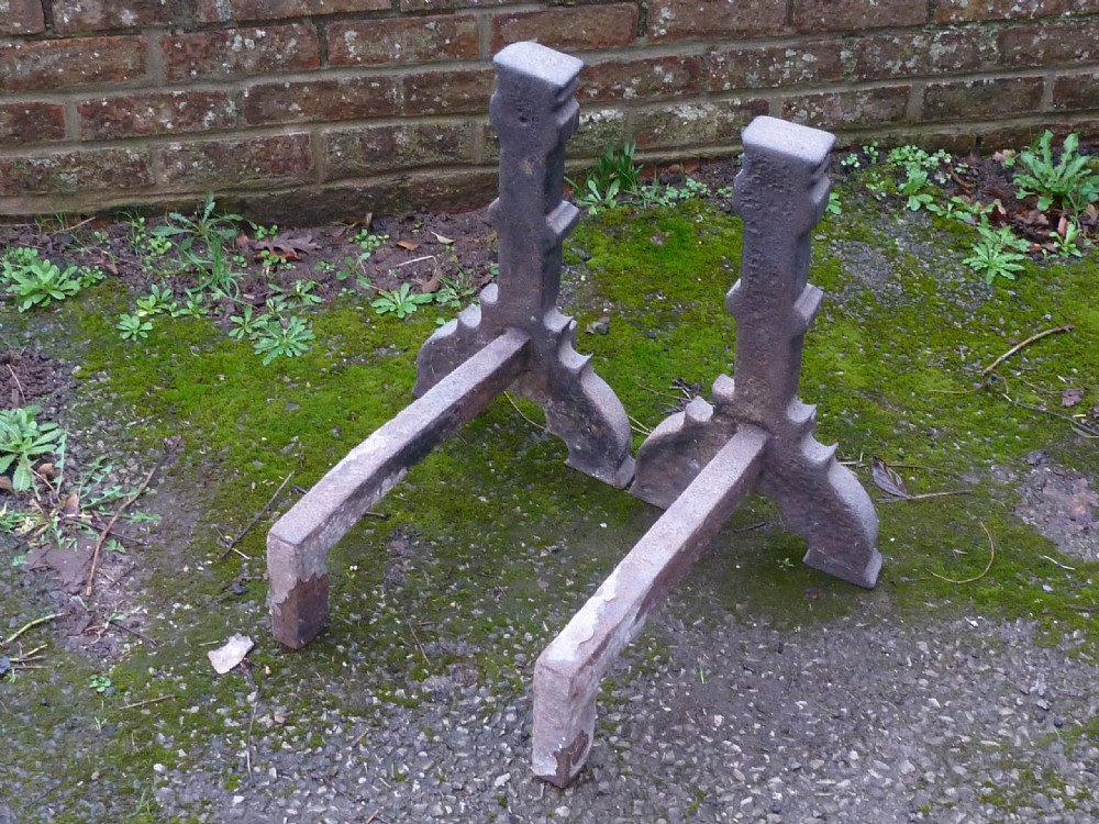 A pair of heavy cast iron Elizabethan fire dogs featuring upright columnar shafts, raised date markings, and broad arched legs. View X